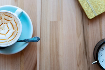 Morning cup of coffee with clock and notebook on a wooden background with copy space. Break from work and relax in cafe. Top view and flat lay.