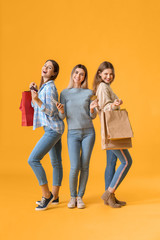 Young women with mobile phone and shopping bags on color background