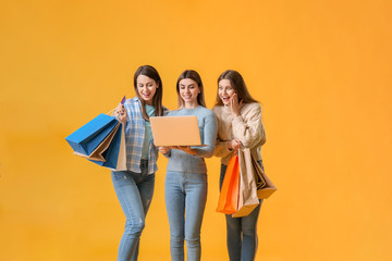 Young women with laptop and shopping bags on color background