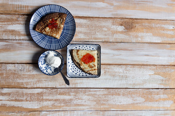 Pancakes on plate with red caviar and sour cream on wooden background