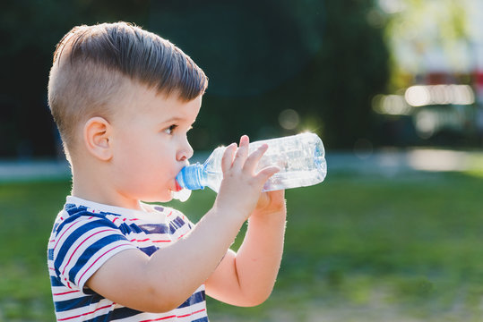 Handsome Boy Drinks Clear Water From A Bottle On A Sunny Day Outside