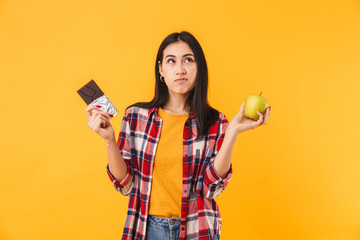 Image of confused caucasian woman holding apple and chocolate