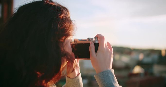 Closeup profile portrait of curly brunette young female using analog camera outdoor urban, natural beauty teenage girl hobby time taking photo picture of city view landscape outside on rooftop
