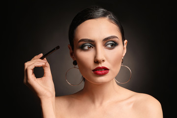 Beautiful young woman applying makeup against dark background