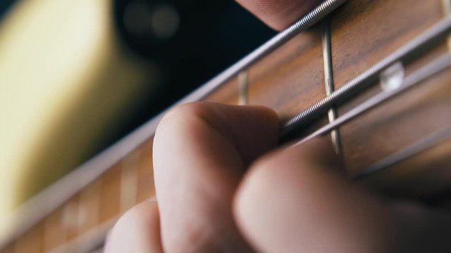 CU: funky artist fingers play bass guitar with pitch shift technique on metal strings over brown neck extreme close view