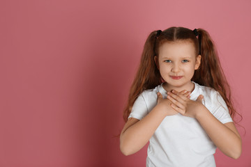 Cute grateful little girl with hands on chest against pink background. Space for text