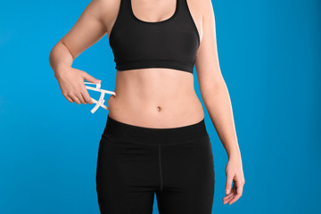 Young woman measuring body fat with caliper on blue background, closeup. Nutritionist's tool