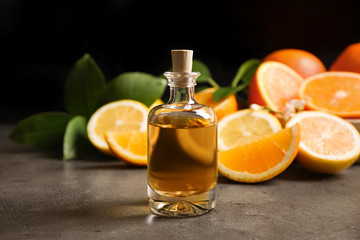Bottle of essential oil and citrus fruits on grey table