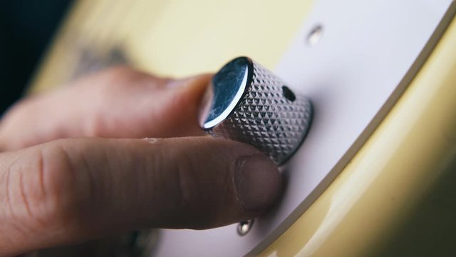 CU: professional guitarist hand rotates volume control knob on white bass guitar pick guard extreme close view