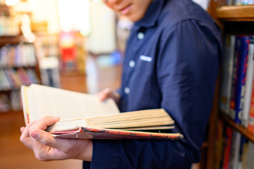 Smart Asian man university student reading book by vintage bookshelf. Textbook resources in college...