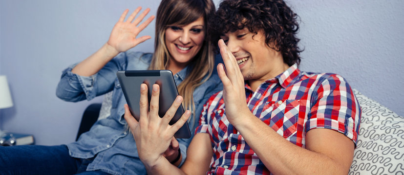 Young couple making a video call with the tablet sitting on the bed - Powered by Adobe