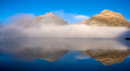 Mountain lake at sunrise in autumn. Landscape with lake, gold sunlight, blue fog over the water, reflection, trees with colorful leaves