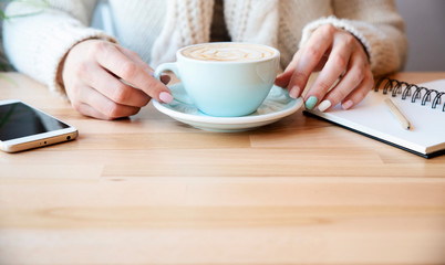 Cup of coffee and woman's hands with phone and notebook on a wooden table with copy space. Freelance and business meeting. Banner.