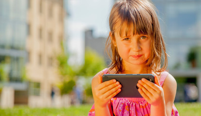 Psychological image of cute little girl addicted to likes: Social networks feeds her neediness. Close up portrait of sad child with mobile smart phone.