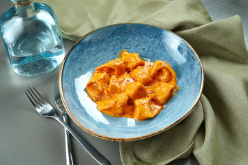 Appetizing orange ravioli in a sauce with different fillings (meat, fish) in a blue bowl on a wooden background. Italian cuisine. Close up