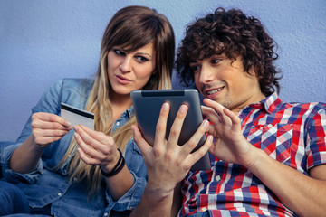 Young man making a purchase on-line with the tablet while his wife looks at him worried