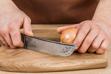 A male cook peels onions with a knife in close-up. The concept of organic cooking