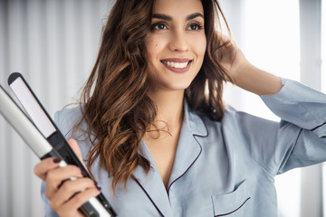 Happy beautiful woman holding curling iron at home