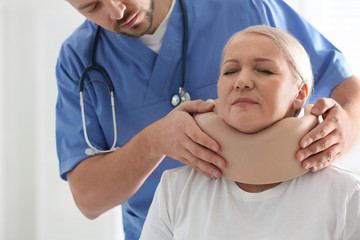 Orthopedist applying cervical collar onto patient's neck in clinic, closeup - Powered by Adobe