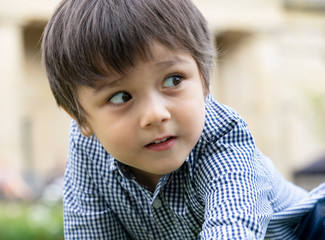 Little Child boy with smiling face sitting in the park with blurry  natural bokeh background, Portrait  of happy kid playing outdoors in spring or summer.