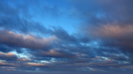 Naklejka na ściany i meble Dark clouds lit by the evening sun with gleams of blue sky.