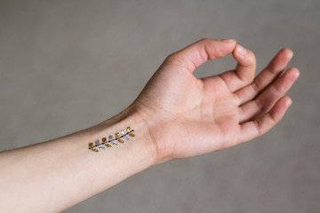 hand of a young woman in meditation hand position wih gold floral leaves temporary tattoo on her...
