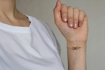hand of a young woman wih gold sailors knot temporary tattoo on her wrist