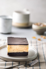 Piece of cake with souffle Birds milk, biscuit, mousse and dark chocolate on a white plate, light background