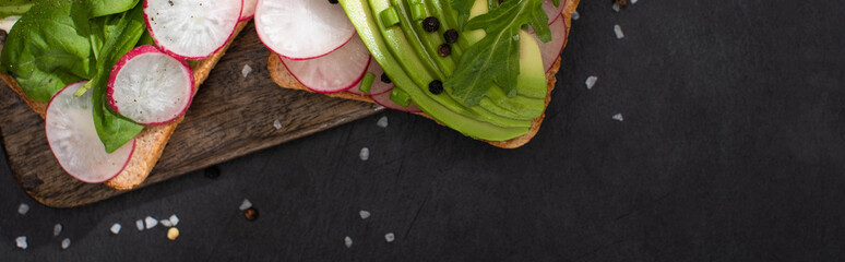 panoramic shot of healthy sandwiches with fresh radish and avocado on wooden board with pepper and salt