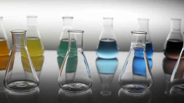 Empty and mixed color liquid filled erlenmeyer flasks reflecting on table