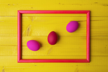 Pink Easter eggs in picture frame on yellow wooden background