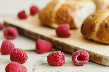 Fresh raspberry and hot cross buns, traditional Easter treat, on background