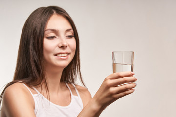 Young beatiful girl hold water glass. Hydrate female face. Happy women indoors. Morning routine. Pretty portrait.