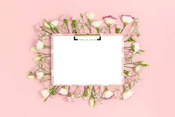 Clipboard mockup with blank paper card. Frame made of flowers on a pink pastel background.