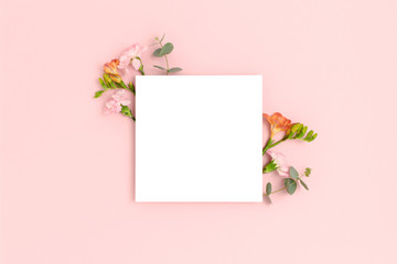 Blank paper card mockup with frame made of flowers and eucalyptus. Festive floral composition with copy space on a pink pastel background.