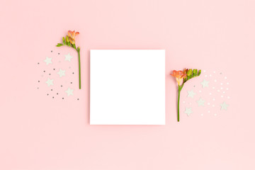 Blank paper card mockup with freesia flowers and stars confetti. Festive concept with place for text on a pink pastel background.