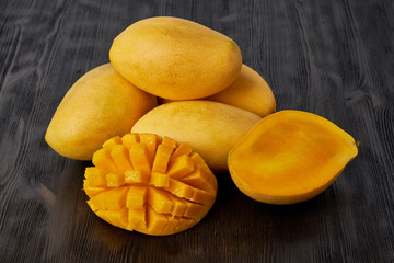 Four whole mango fruits on wooden table and cut into slices. Large juicy bright ripe yellow fruits
