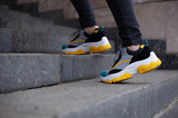 Feet  shod in sneakers multi-colored yellow, white, black and blue climb the marble stairs