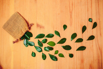 Green leaves on the wooden background. Leaves falling from the bag.