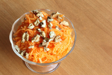 Carrot salad with orange and walnut in a glass plate on a brown background