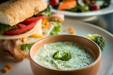 Broccoli soup on a bowl with sandwich on the background.