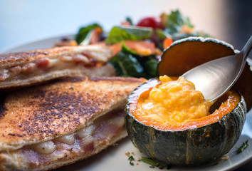 A spoonful of pumpkin soup in a mini pumpkin shell. Toast bread for brunch with vegetables.