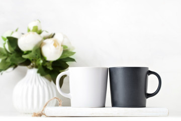 Obraz na płótnie Canvas White and black mugs on a background of flowers . Mock up. Template Space for Creative Artwork Lettering Text Product Promotion Branding. Elegant style.