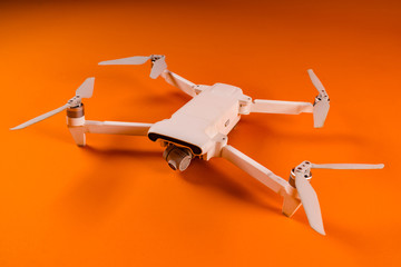 Close-up of white drone on orange background. Modern drone unmanned aerial vehicle with propellers.