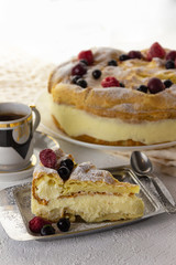 Piese of custard pie with custard cream and frozen berries on a  background with whole cake and cup of coffee. Carpathian pie. Karpatka pie.