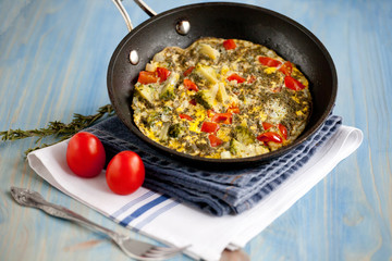 Frittata with broccoli, sweet peppers, tomatoes and herbs in skillet. Italian style omelette with vegetables