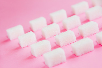 square small white cubes of refined sugar on a pink background