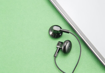 Black smartphone with a white border (stripe) in a circle. Gray blank screen. and two black small earbuds from the headset for insertion into the ear. Part of the phone on a green isolated background