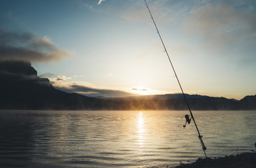 fishery relax concept, outline fishing rod at sunrise sunlight, hobby sport on mist evening lake, catch fish on river on background night sky foggy mount