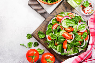 Spring vegan salad with spinach, cherry tomatoes, corn salad, baby spinach, cucumber and red onion. Healthy food concept. Gray stone table. Top view. Copy space